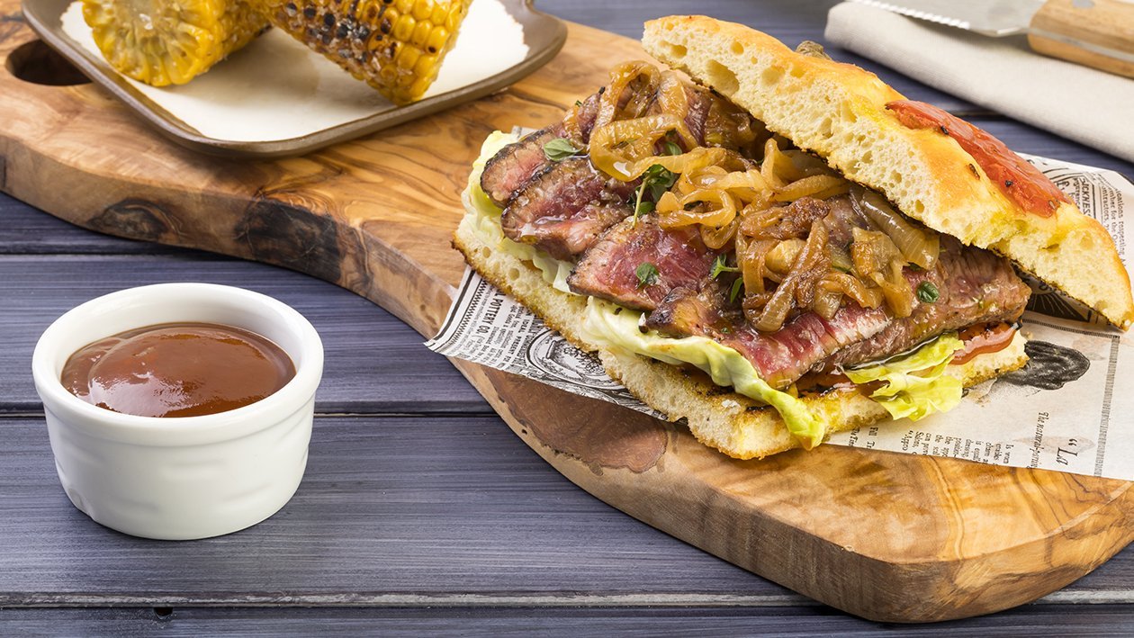 Focaccia di patate con tagliata di manzo laccato alla BBQ dolce e sambuca con pannocchia di mais al sale maldon e cipolle arrostite al rosmarino – Ricetta Focaccia di patate con tagliata di manzo laccato alla BBQ dolce e sambuca con pannocchia di mais al sale maldon e cipolle arrostite al rosmarino – Ricetta